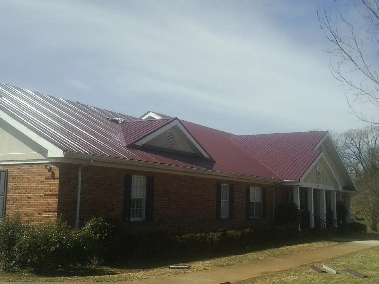 Red metal roof with gabled entries on a long brick building, from a Hail Damage Roof Repair job in Rockton