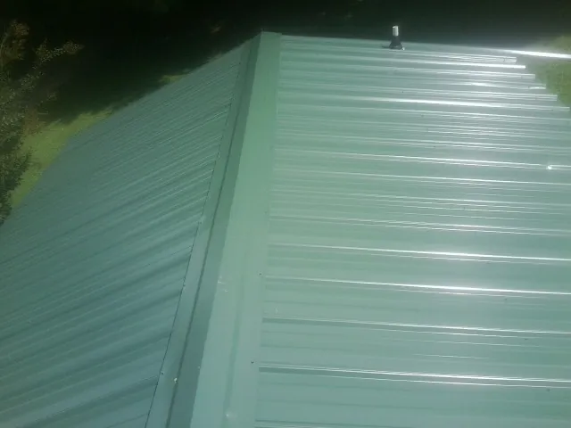 New green metal panels meeting at the ridge of a roof — Flat Roof Repair work by our crew in Rockton