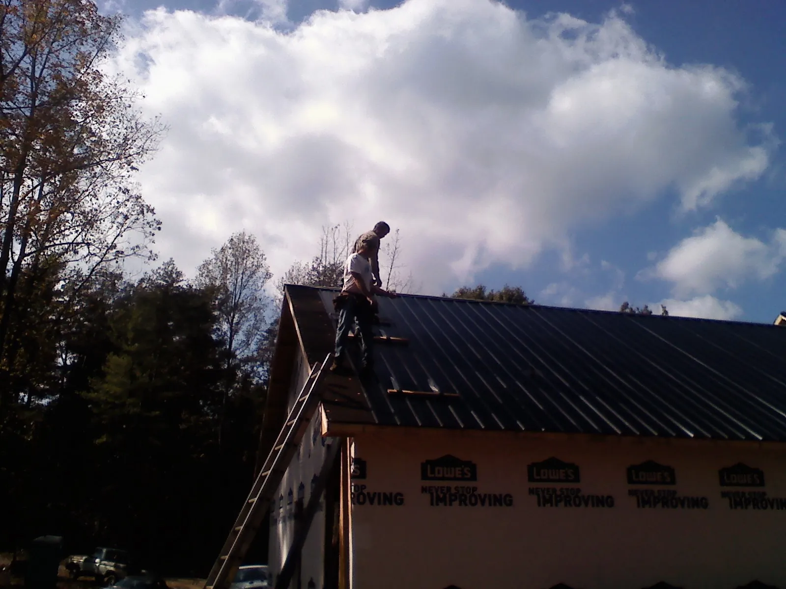 Roofer fastening dark metal panels high against a cloudy sky, from a Roof Inspection job in Rockton